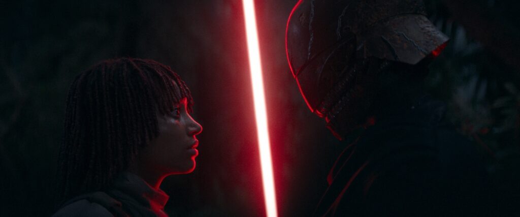 Osha stands face to face with the masked Master (Qimir). Qimir's red lightsaber is ignited between them.