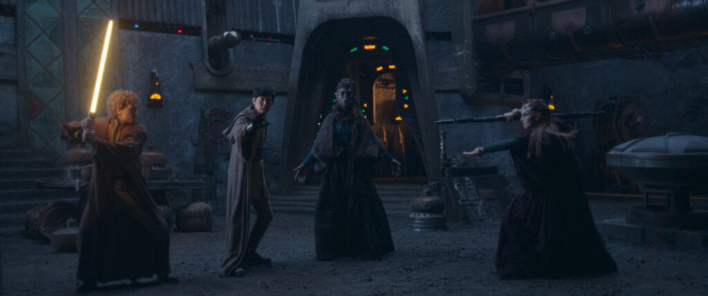 Torbin raises his yellow lightsaber against a threat from Mother Koril. Sol and Mother Aniseya try to stop them.