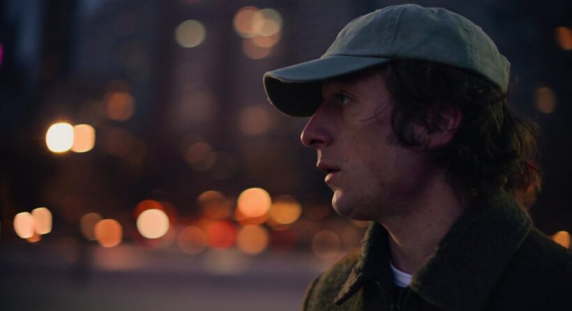 Carmy wearing a baseball cap stares out at the lake in the early morning light.