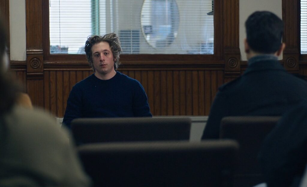 Carmy sits at the front of an Al-Anon group in a church room.