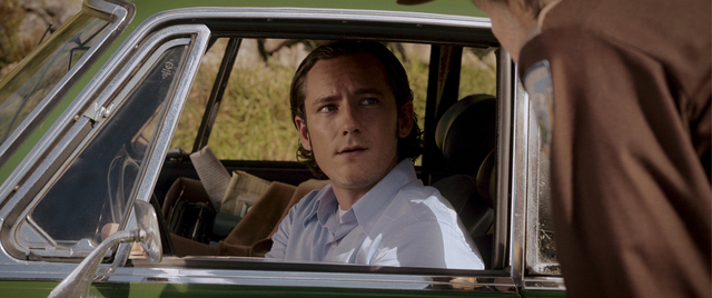 Ben Mears sits in the driver's seat of a green car and looks out the side window at the sheriff. 