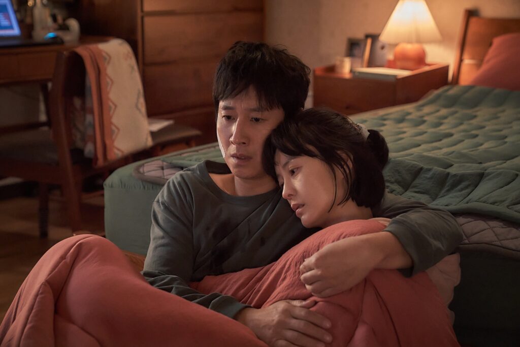 Hyun-su holds Soo-jin at the foot of their bed. They both look scared.