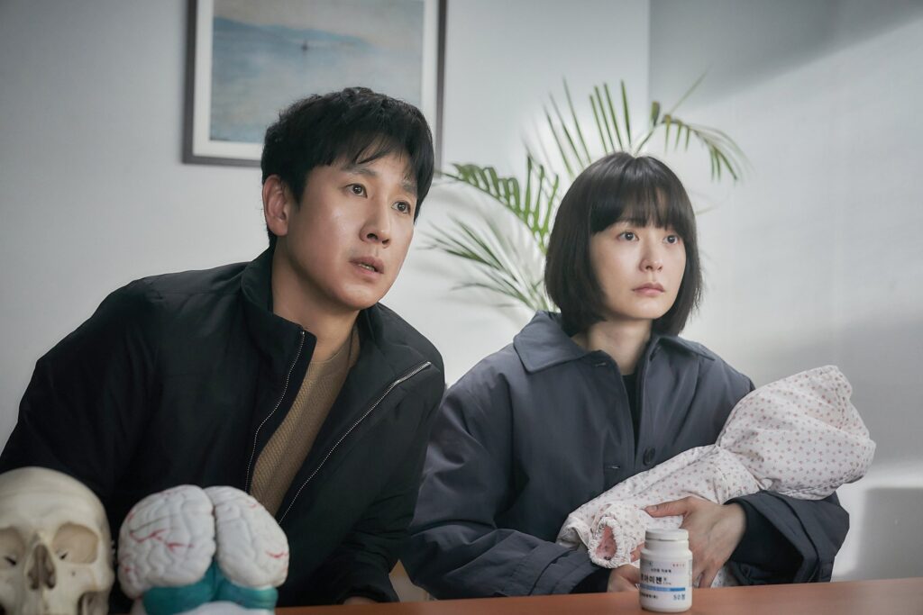 Hyun-su and Soo-jin sit in a doctor's office. Soo-jin holds their newborn baby.