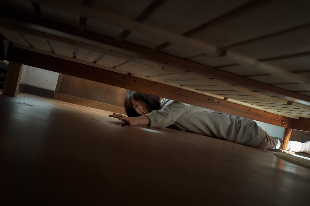 Soo-jin lies on the floor and reaches a hand out under the bed.