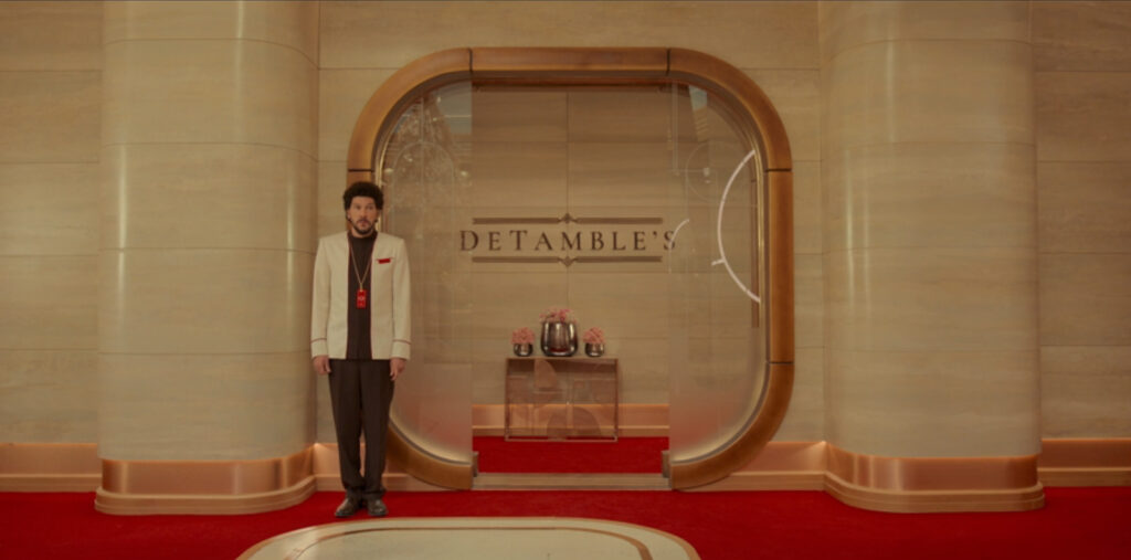 Trev, in a white jacket and black undershirt and trousers, stands outside the entrance to a bar named "DeTamble's" in the Time Hotel