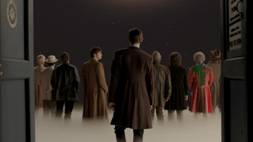 The Doctors- visibly 4 through 11 and the War Doctor- in a dream like sequence stand with their backs to the camera looking up at Gallifrey.