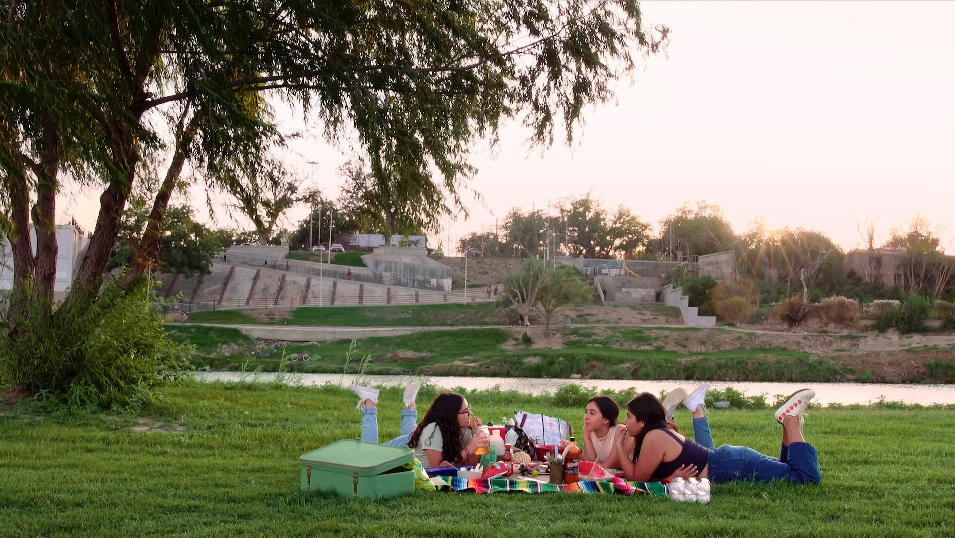 Three young girls have a picnic on the Texas side of the Rio Grande. Piedras Negras can be seen across the river.