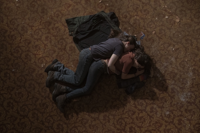 Ellie lies on a floor curled around Dina, her arm wrapped around the other woman.