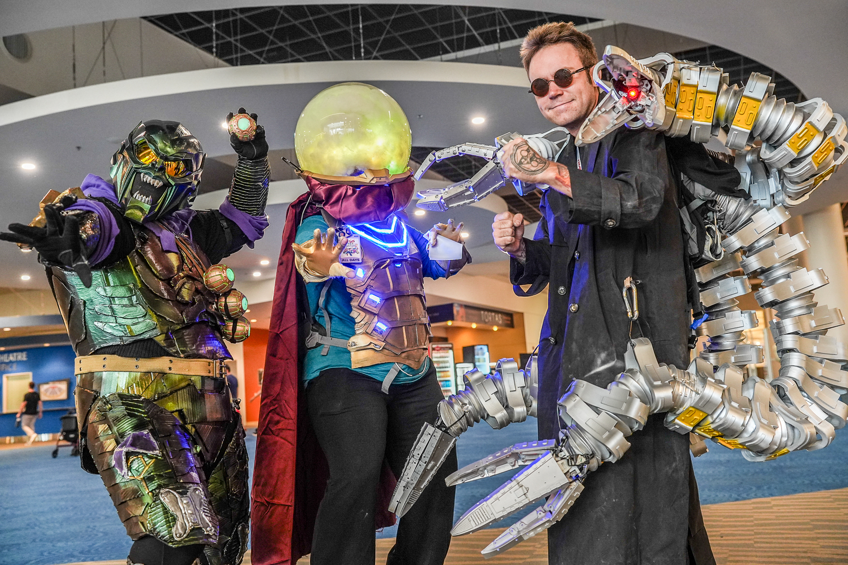 Three attendees dressed as Spider-Man villains Green Goblin, Mysterio, and Doctor Octopus pose together at Fan Expo Denver, showcasing detailed, illuminated cosplay costumes with mechanical tentacles, armor, and special effects.
